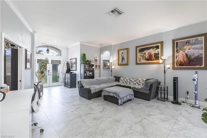 Living area with ornamental molding, arched walkways, and french doors