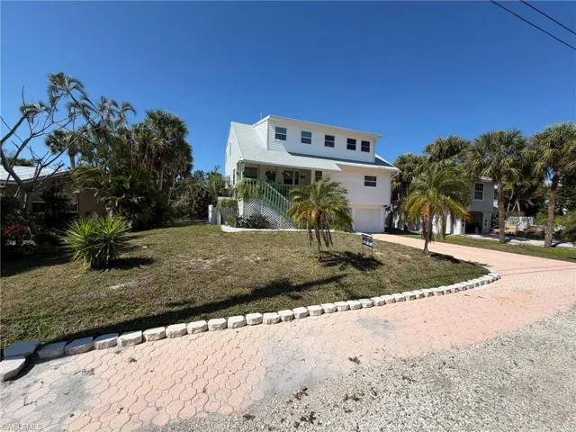 Coastal home with an attached garage, a front lawn, driveway, and covered porch