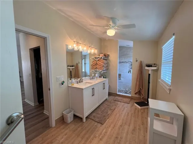Bathroom featuring double vanity, a stall shower, ceiling fan, wood finished floors, and a sink