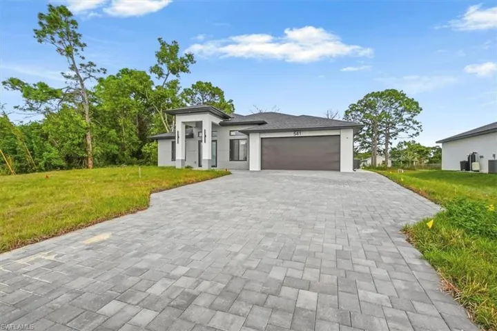 Prairie-style house featuring a front yard, an attached garage, decorative driveway, and stucco siding