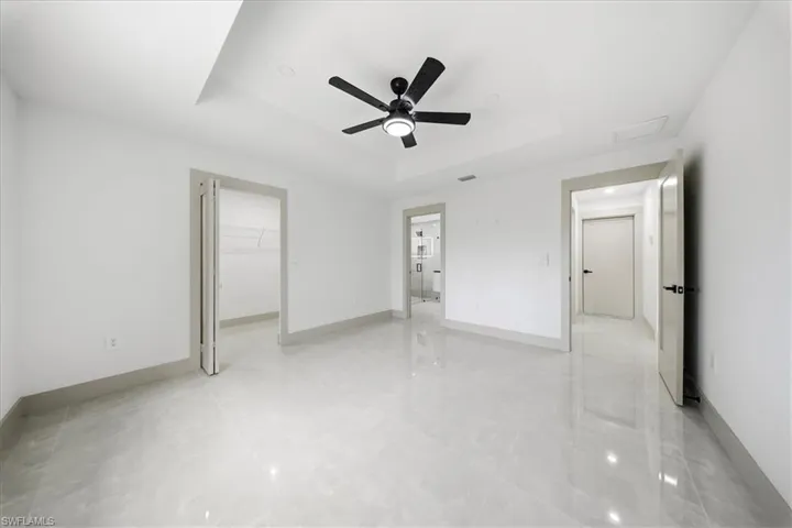 Unfurnished bedroom with a spacious closet, a tray ceiling, ceiling fan, and light tile patterned floors