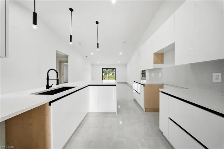 Kitchen featuring white cabinets, modern cabinets, light stone counters, and lofted ceiling
