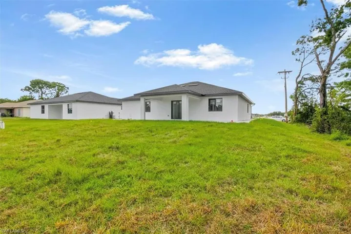 Rear view of house with a lawn, stucco siding, and a patio