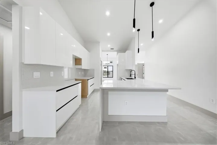 Kitchen with modern cabinets, light stone countertops, white cabinets, and pendant lighting