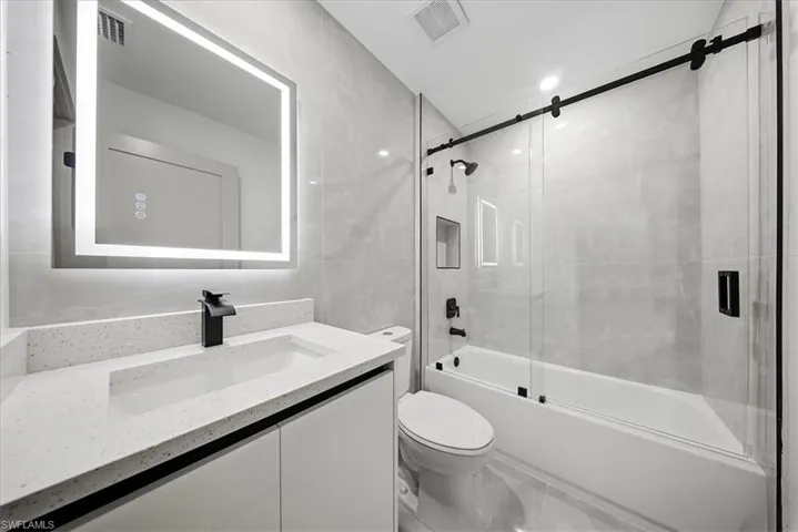 Full bath with vanity, tile walls, and enclosed tub / shower combo