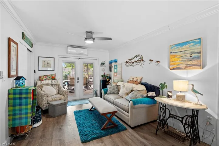 Living room featuring french doors, crown molding, wood-type flooring, a wall unit AC, and ceiling fan