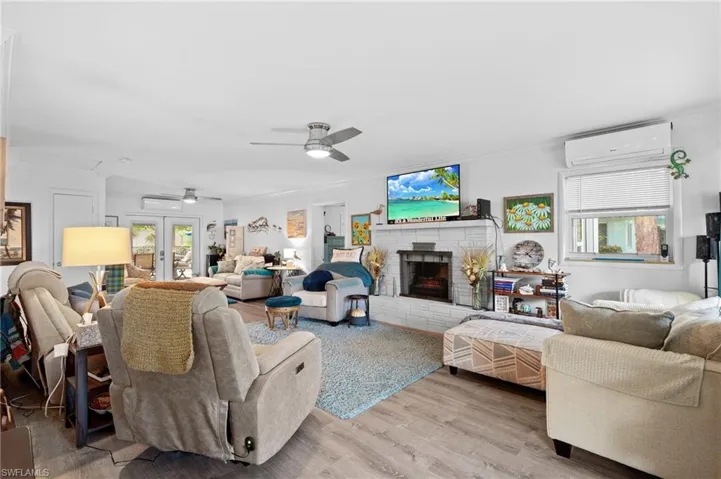 Living room with plenty of natural light, a wall mounted air conditioner, light wood-type flooring, and french doors