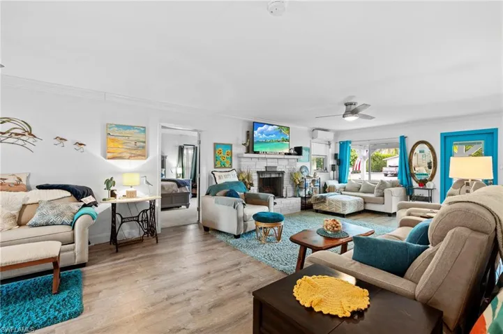 Living room with crown molding, a wall unit AC, ceiling fan, a fireplace, and light hardwood / wood-style floors