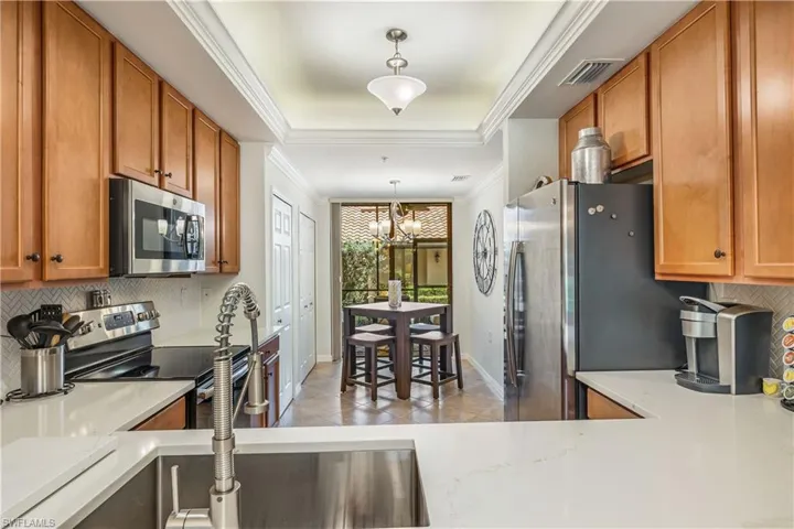 Kitchen with crown molding, tasteful backsplash, a chandelier, appliances with stainless steel finishes, and decorative light fixtures