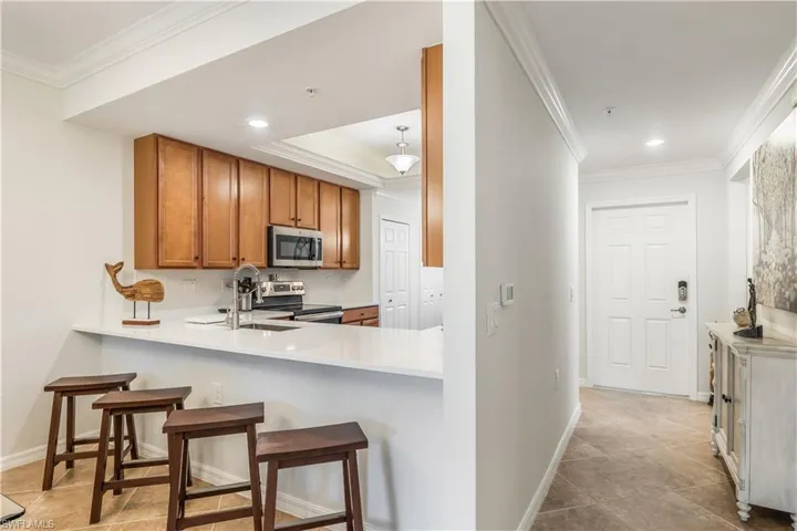 Kitchen with stainless steel appliances, crown molding, sink, light tile patterned floors, and a kitchen breakfast bar
