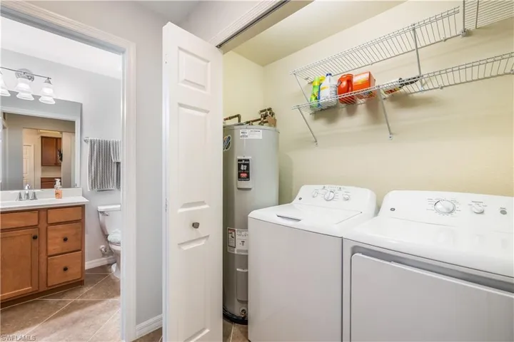 Laundry room with light tile patterned flooring, washing machine and clothes dryer, sink, and water heater