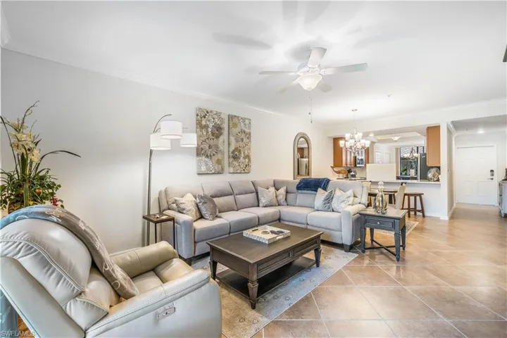 Tiled living room featuring ceiling fan with notable chandelier and ornamental molding
