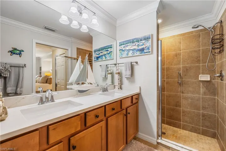 Bathroom featuring walk in shower, dual vanity, crown molding, and an inviting chandelier