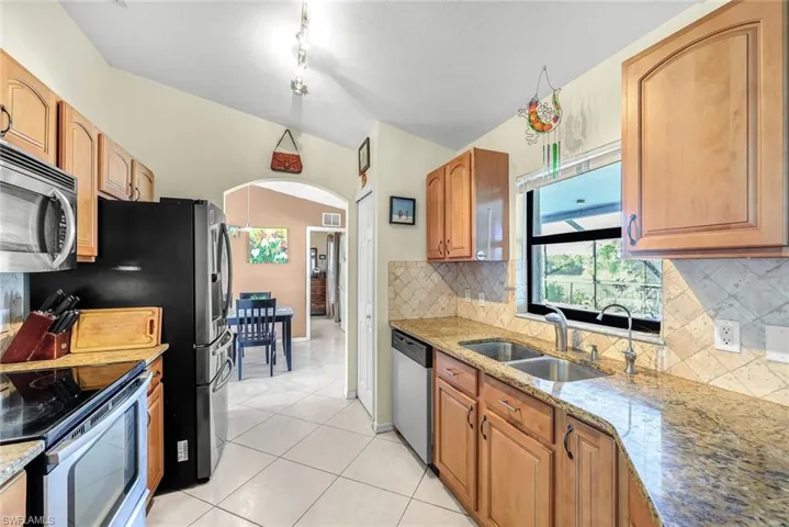 Kitchen featuring light tile patterned floors, stainless steel appliances, tasteful backsplash, a sink, and light stone countertops