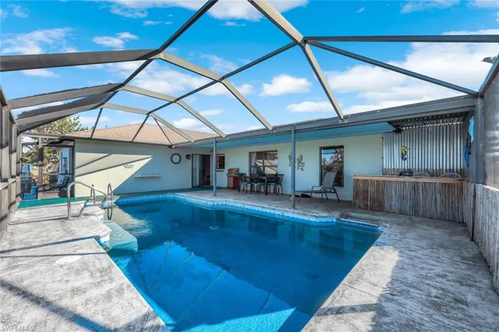 Outdoor pool with a water view, glass enclosure, and a patio area