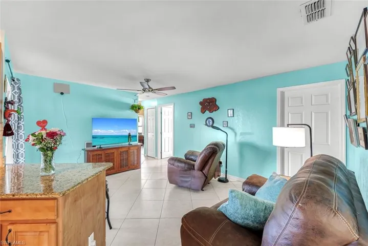 Living room with lofted ceiling, light tile patterned flooring, visible vents, and a ceiling fan