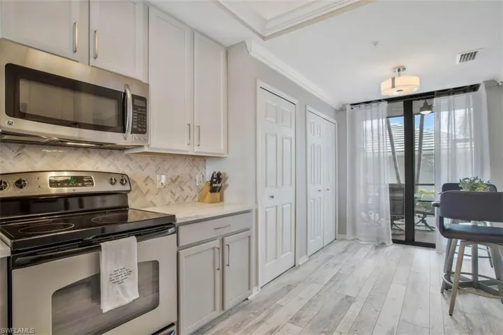 Kitchen featuring light stone counters, light hardwood / wood-style flooring, stainless steel appliances, tasteful backsplash, and ornamental molding