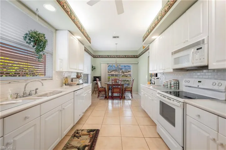 Kitchen featuring sink, light tile patterned floors, pendant lighting, white appliances, and white cabinets