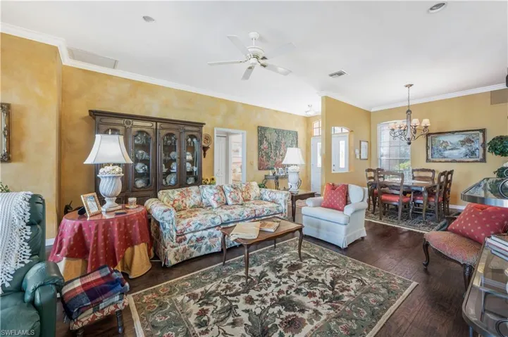 Living room featuring crown molding, ceiling fan with notable chandelier, and dark wood-type flooring