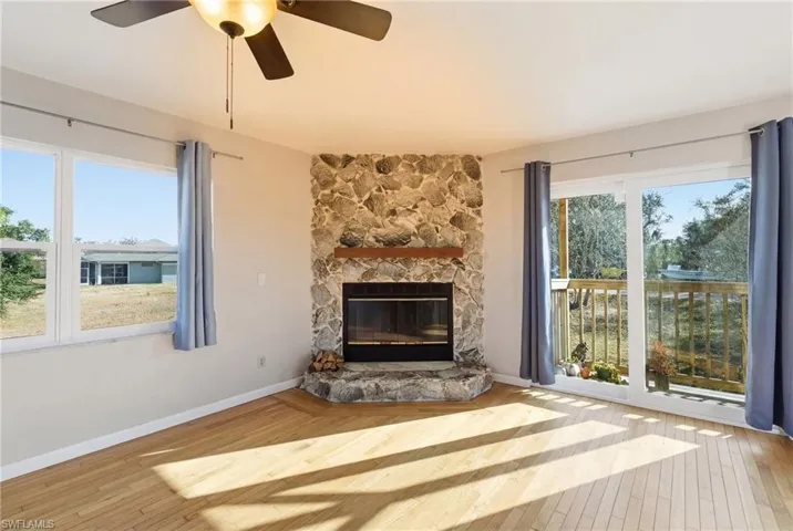 Unfurnished living room with light wood-style floors, a ceiling fan, a stone fireplace, and healthy amount of natural light