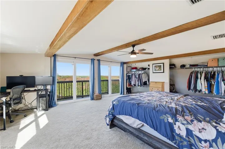 Bedroom with an office area, carpet, access to outside, lofted ceiling with beams, and a ceiling fan