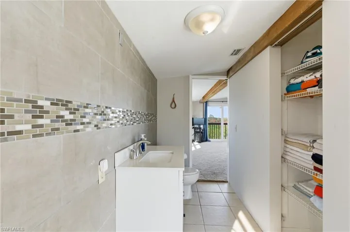 Half bathroom featuring vanity, light tile patterned flooring, light colored carpet, tile walls, and a closet