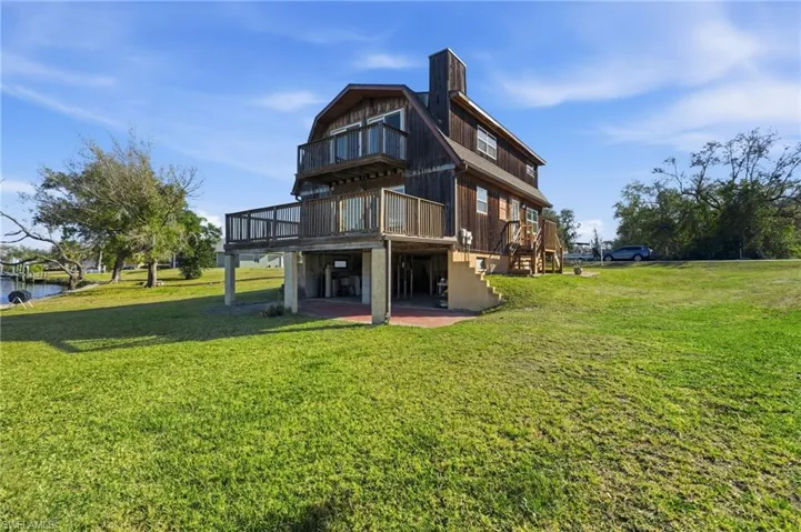 Back of house with a chimney, a lawn, a patio area, a deck, and a gambrel roof