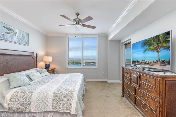 Bedroom featuring light colored carpet, ornamental molding, baseboards, and a ceiling fan