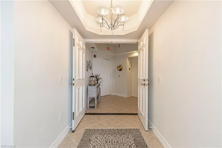 Hallway featuring light tile patterned floors, a chandelier, baseboards, and a raised ceiling
