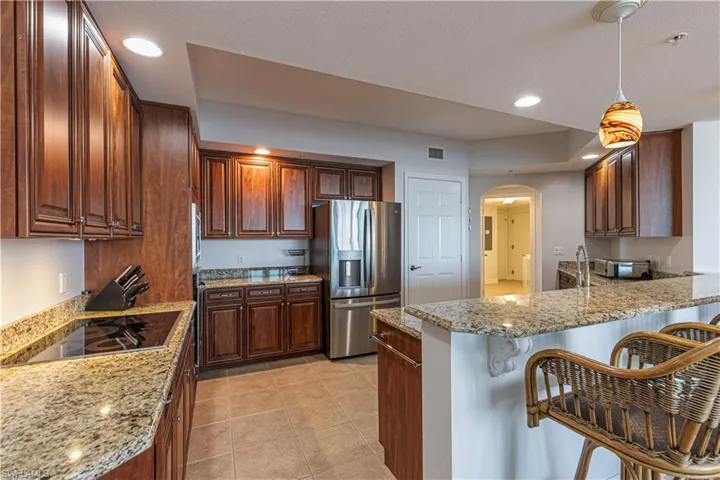 Kitchen with appliances with stainless steel finishes, a peninsula, arched walkways, a breakfast bar area, and light stone counters