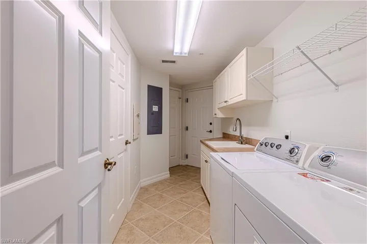 Laundry area featuring washing machine and clothes dryer, cabinet space, electric panel, light tile patterned floors, and baseboards