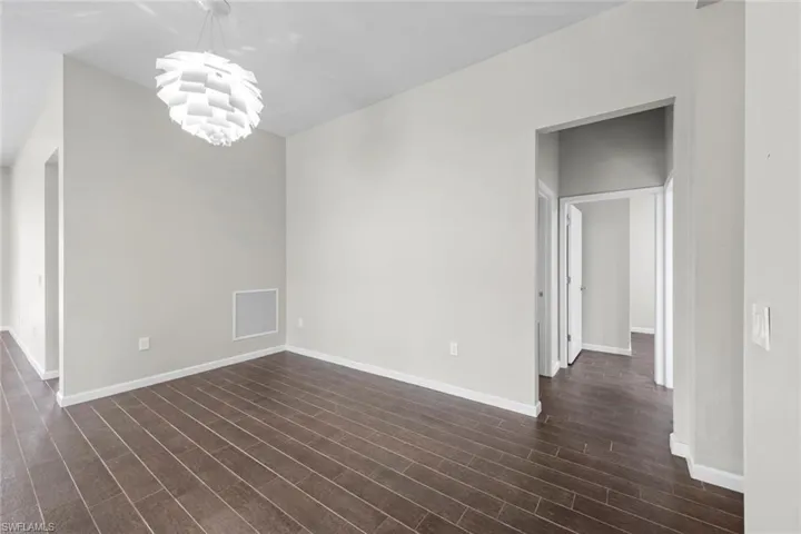 Unfurnished room featuring dark wood-style floors, visible vents, a notable chandelier, and baseboards