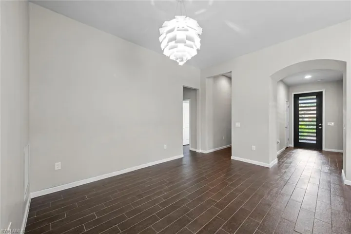 Unfurnished room with a notable chandelier, dark wood-type flooring, arched walkways, and baseboards