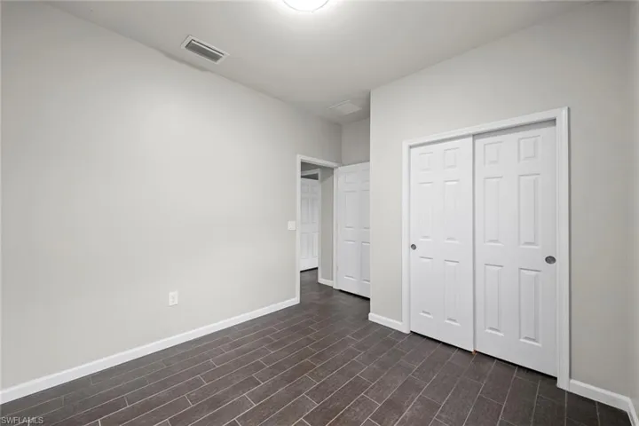 Empty room featuring dark wood-style flooring, visible vents, baseboards, and ceiling fan