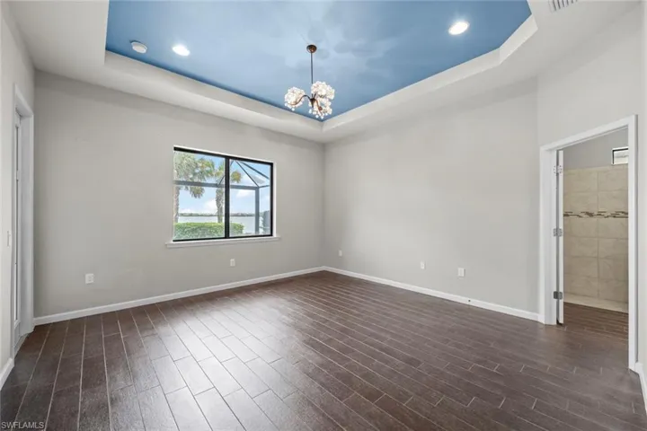 Empty room featuring a tray ceiling, baseboards, dark wood-type flooring, and a chandelier