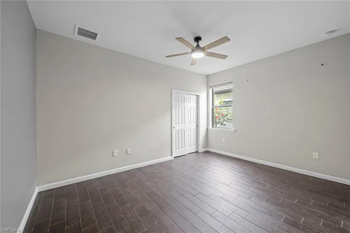 Unfurnished room with dark wood-style floors, baseboards, ceiling fan, and visible vents