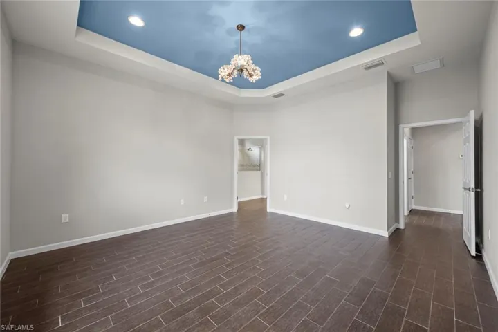 Spare room featuring a tray ceiling, visible vents, a chandelier, and dark wood finished floors