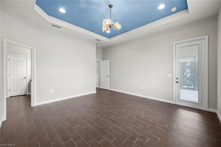 Unfurnished room with a raised ceiling, a notable chandelier, dark wood-style floors, and visible vents