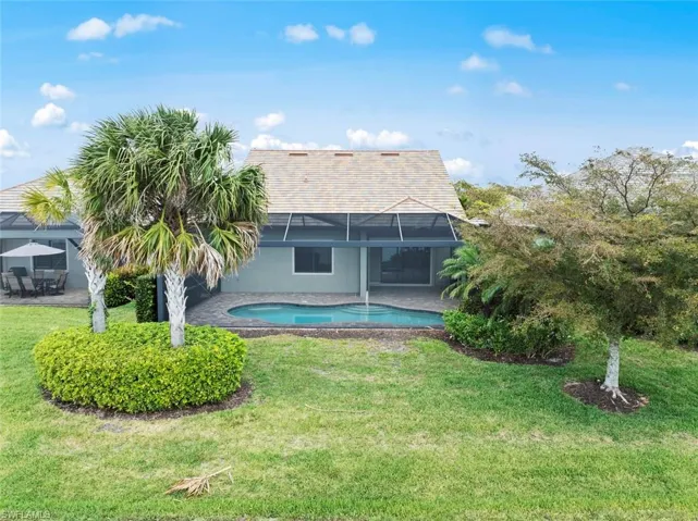 Back of house with stucco siding, a lanai, a patio, a lawn, and an outdoor pool