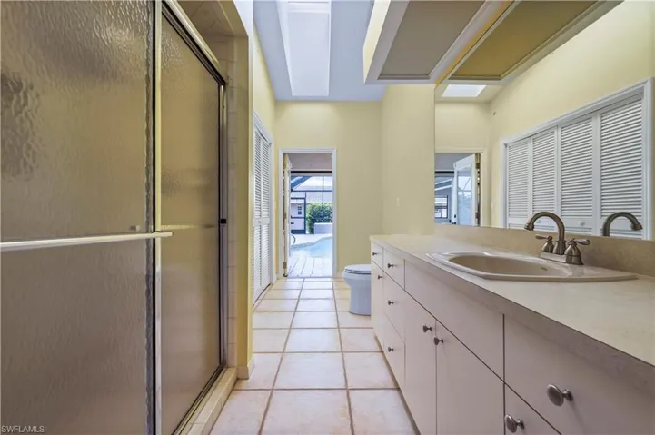 Bathroom featuring a shower with door, vanity, toilet, tile floor, door to lanai