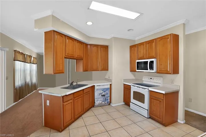 Kitchen with crown molding, white appliances, light countertops, brown cabinetry, and light tile patterned floors