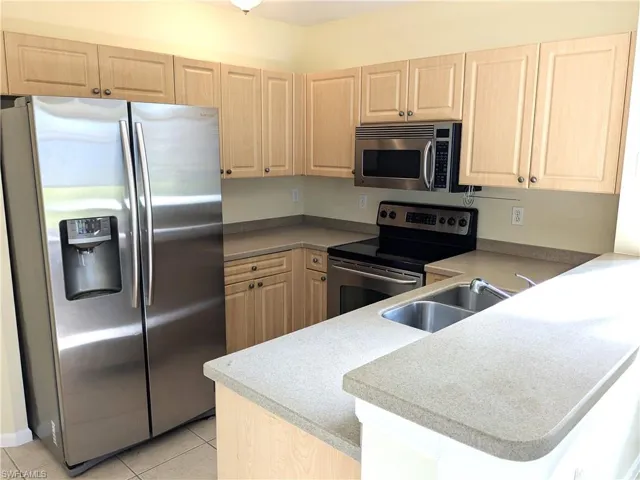 Kitchen with light tile patterned floors, a sink, a peninsula, light brown cabinets, and appliances with stainless steel finishes
