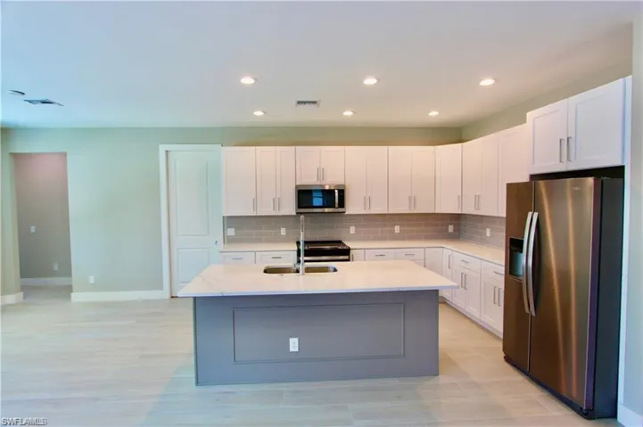 Kitchen featuring white cabinets, stainless steel appliances, tasteful backsplash, an island with sink, and light stone counters