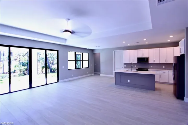 Kitchen with an island with sink, tasteful backsplash, black fridge, white cabinets, and sink