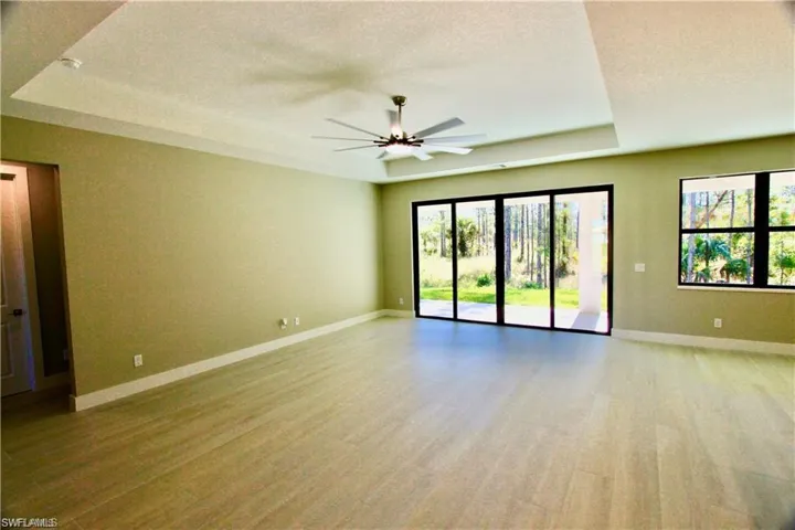 Spare room with a textured ceiling, ceiling fan, light wood-type flooring, and a tray ceiling