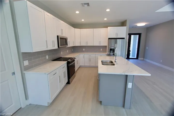 Kitchen featuring light hardwood / wood-style floors, white cabinetry, a kitchen island with sink, light stone countertops, and appliances with stainless steel finishes