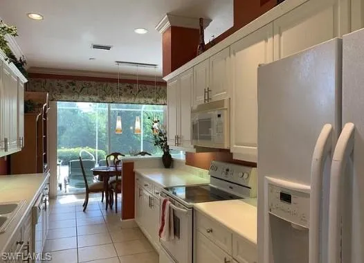 Kitchen featuring white appliances, white cabinets, ornamental molding, light tile patterned floors, and decorative light fixtures