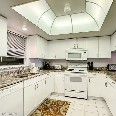 Kitchen with white appliances, light tile patterned floors, and white cabinets