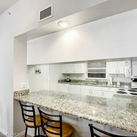 Kitchen featuring white cabinets, light stone counters, and a breakfast bar area