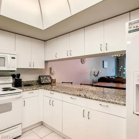Kitchen featuring white appliances, white cabinetry, light tile patterned flooring, and light stone countertops